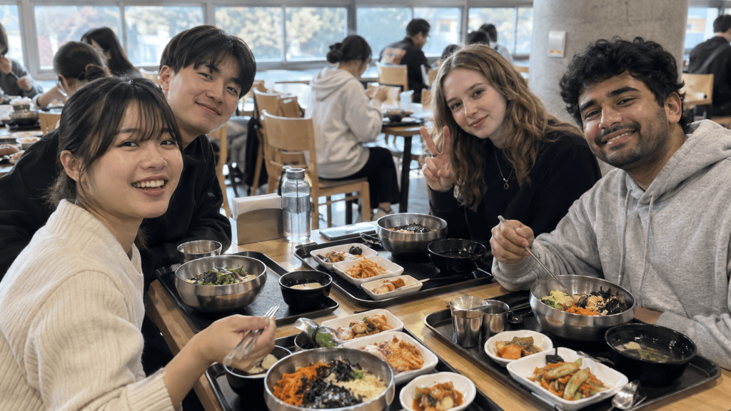 A group of four friends enjoying a meal together in a restaurant, smiling and posing for the camera, with various dishes on the table.