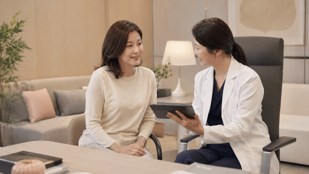 A healthcare professional in a white coat smiles while showing a tablet to a patient in a cozy consultation room.